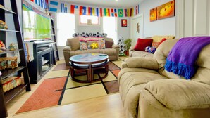 Un salon avec un canapé, une table basse et un téléviseur. Il y a des drapeaux accrochés au mur et un tableau.