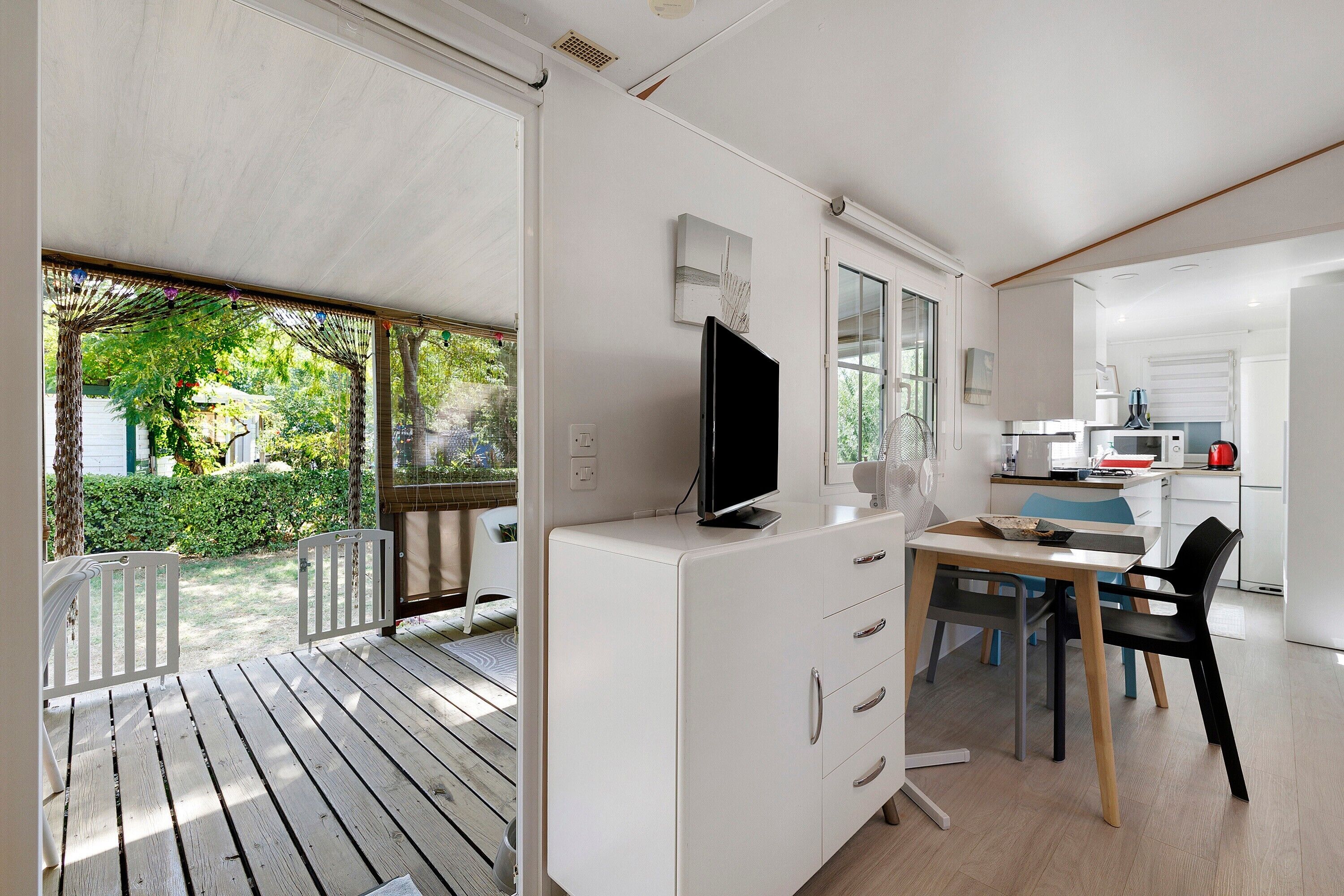 Eine moderne Küche mit weißen Schränken, ein Essbereich mit Tisch und Stühlen sowie ein großes Fenster mit Blick auf einen Garten.