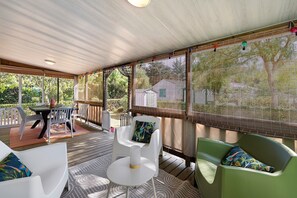 A covered outdoor area with a table and chairs, a view of greenery through the windows, and a wooden deck.