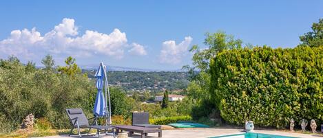 A swimming pool with lounge chairs and an umbrella, surrounded by greenery and a view of a town.