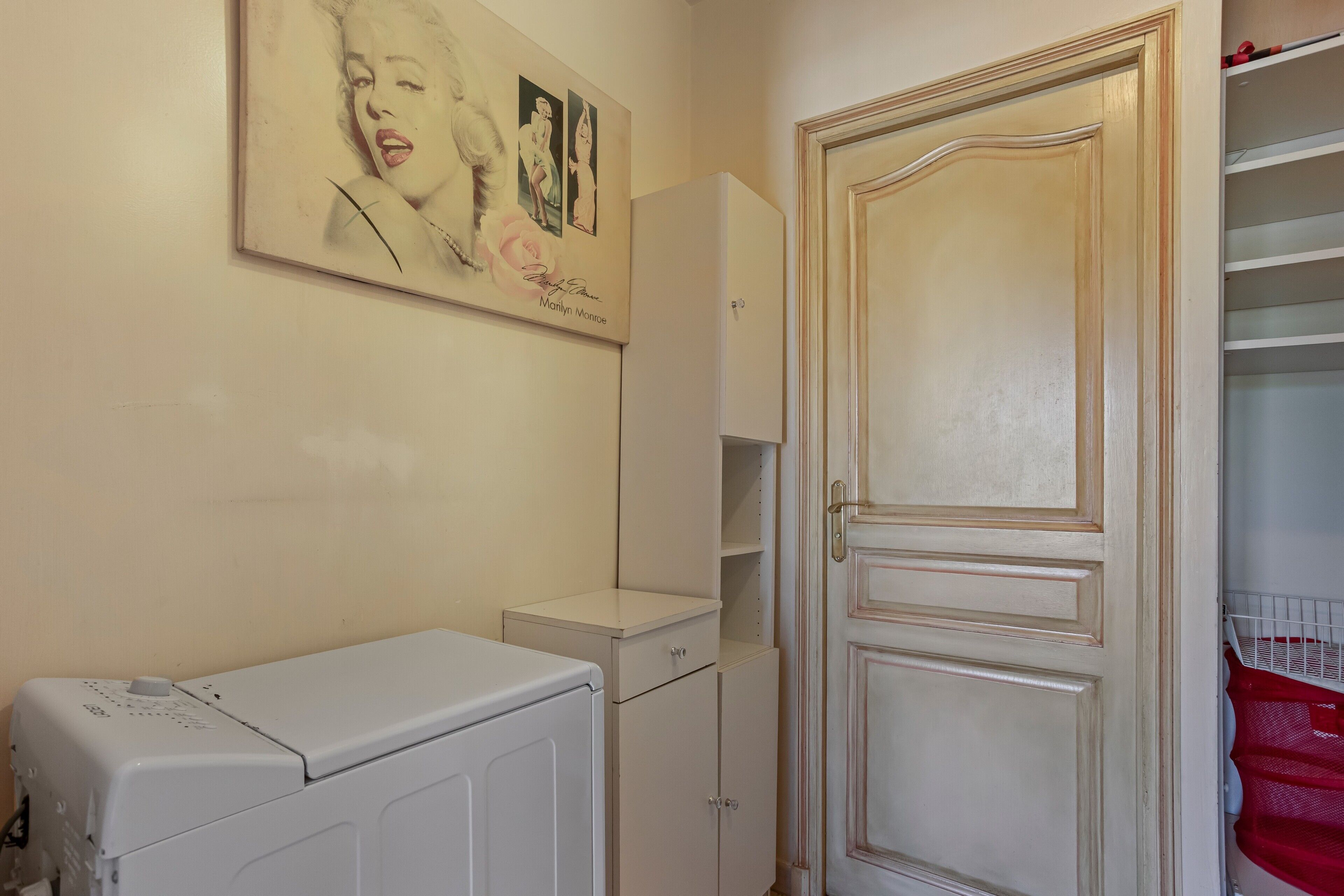 A bathroom with a washing machine, a cabinet, and a door with a mirror.