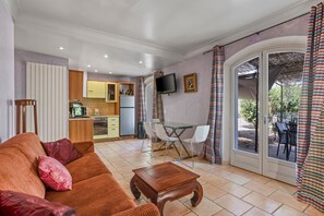 Un espacio habitable compacto con sofá, una mesa de centro de madera, una zona de comedor con sillas, una cocina equipada y un televisor montado en la pared.