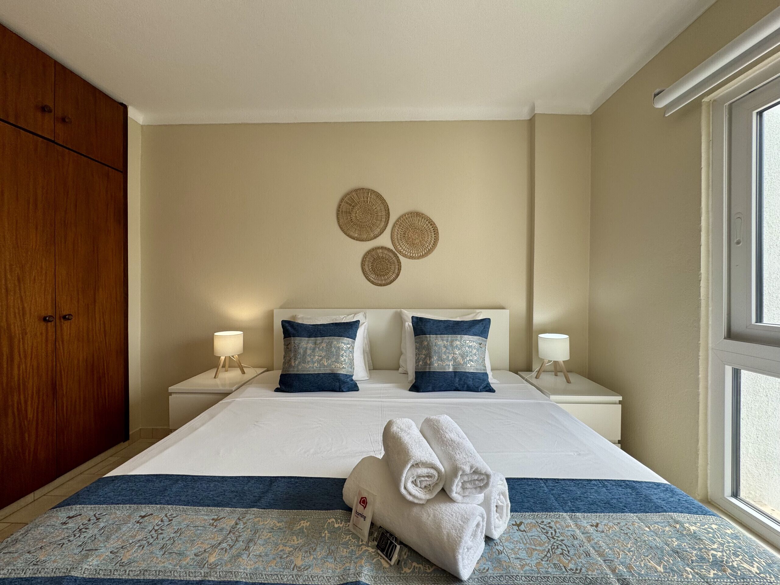 A hotel room with a large bed, two bedside tables with lamps, a wardrobe, and a view of the outdoors.