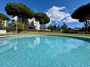 A clear blue swimming pool surrounded by trees and a white building. - VILAMOURA CHARMING 3 WITH POOL by HOMING (Vilamoura)