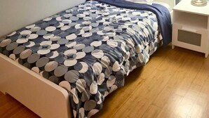 A single bed with a patterned bedspread, a bedside table with a lamp, and a window with curtains.