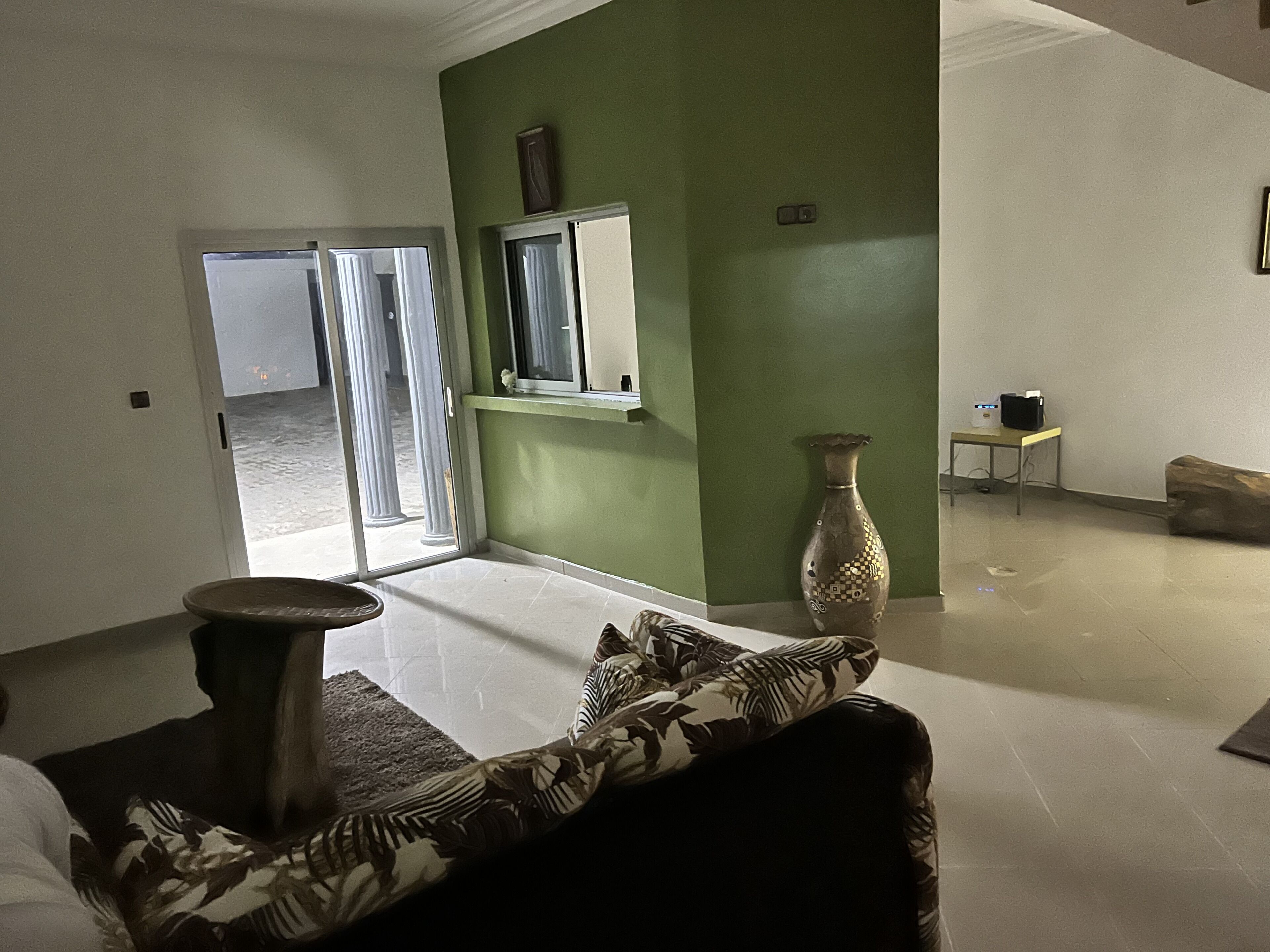Una habitació amb una paret d'accent verd, un gerro gran, un sofà amb coixins estampats i una taula amb un altaveu.