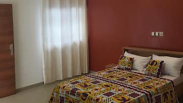 Une chambre à coucher avec un lit, des rideaux, une lampe fixée au mur et un luminaire au plafond.