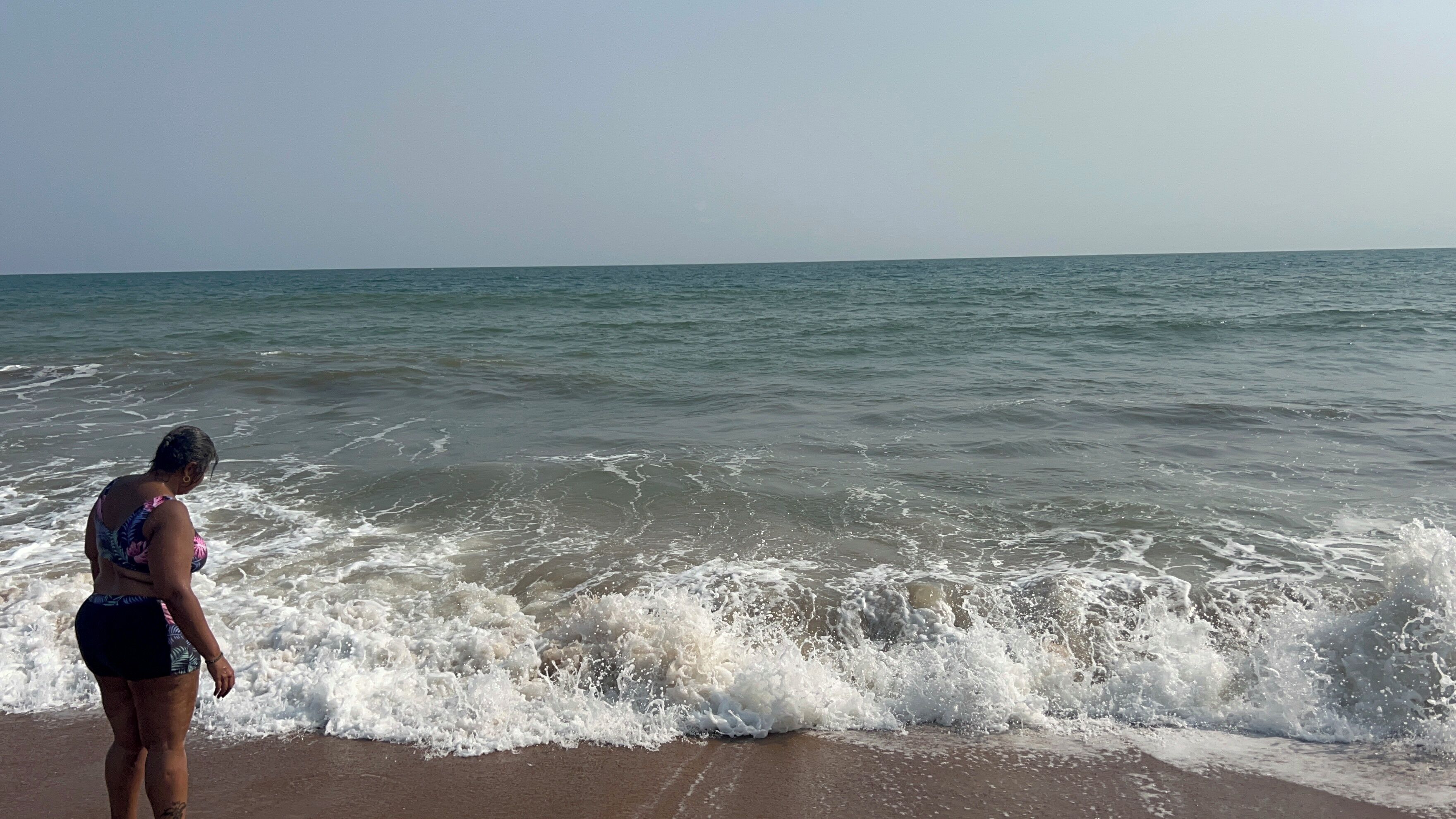 A beach with waves and a person standing on the sand.
