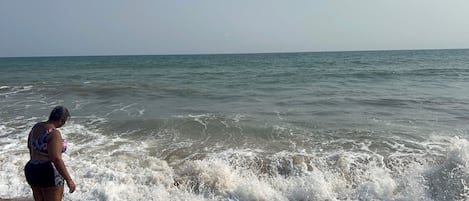 A beach with waves and a person standing on the sand.