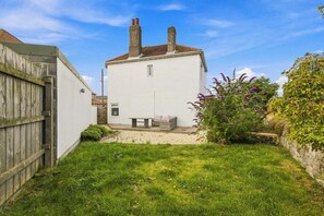 A white house with a chimney, a small patio with a table and chairs, and a grassy yard. - Kilrenny - North East Escapes (Seahouses)