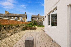 A courtyard with a wooden deck, a stone wall, and a white building with a window. - Kilrenny - North East Escapes (Seahouses)