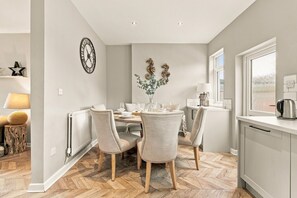 A dining area with a round table, four chairs, a clock on the wall, and a window with a view. - Kilrenny - North East Escapes (Seahouses)