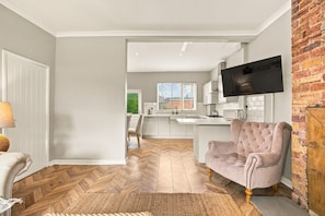 A modern kitchen with white cabinets, a flat-screen TV, and a herringbone wood floor. - Kilrenny - North East Escapes (Seahouses)