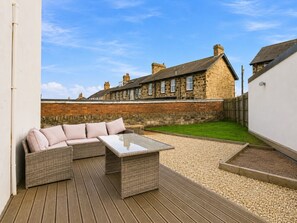 Un espace patio aménagé avec du mobilier d’extérieur, offrant une vue sur un bâtiment en pierre en arrière-plan.