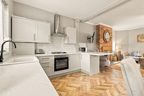 A modern kitchen with white cabinets, a built-in oven, and a herringbone wood floor. - Kilrenny - North East Escapes (Seahouses)