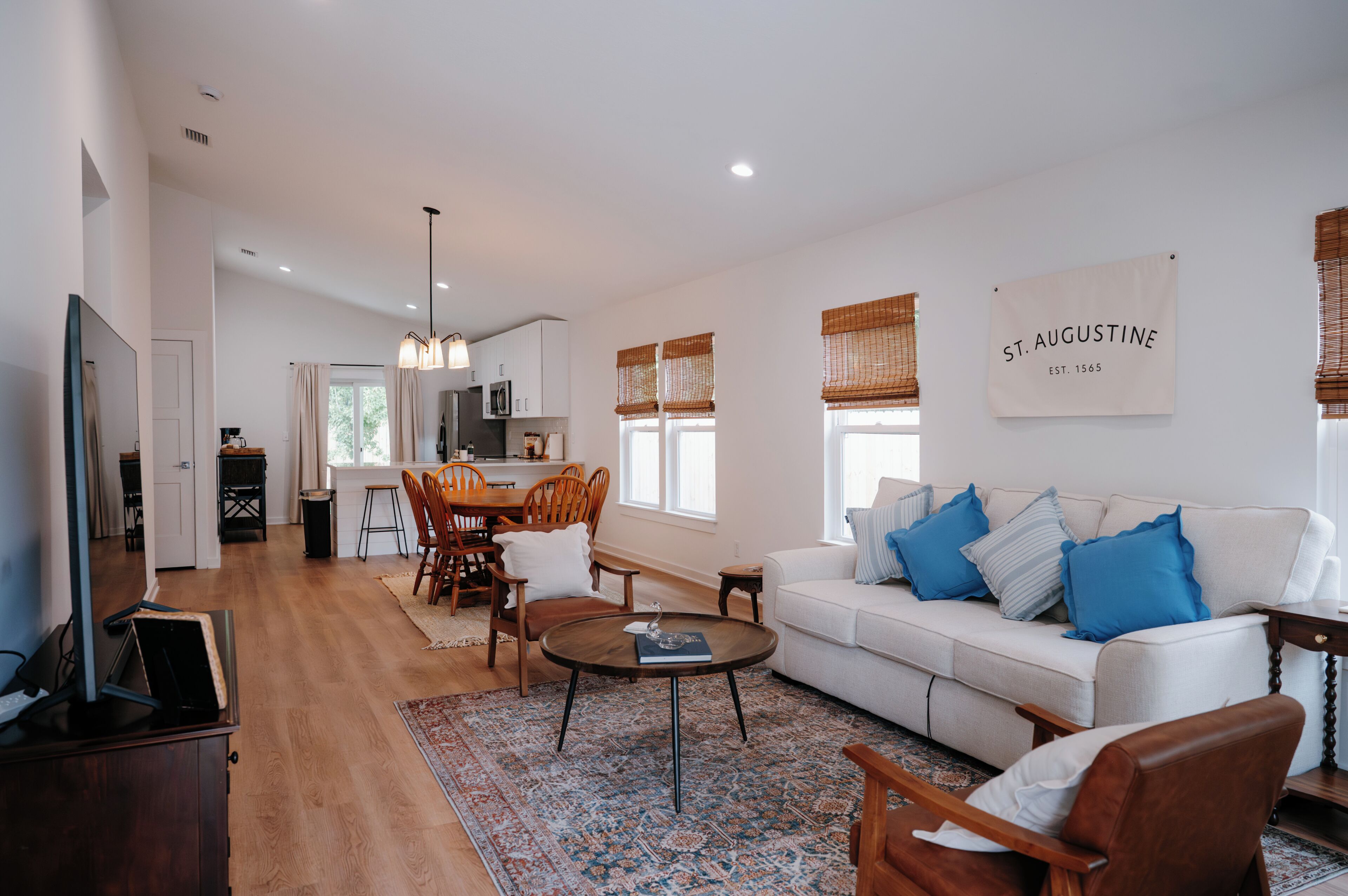 A modern living room with a white sofa, blue cushions, a coffee table, and a dining area with wooden chairs.