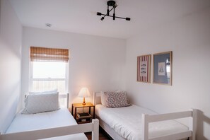 A bedroom with two single beds, a bedside table with a lamp, a window with blinds, and two framed pictures on the wall. - Bright and Cozy St. Augustine Home near Downtown (St. Augustine)