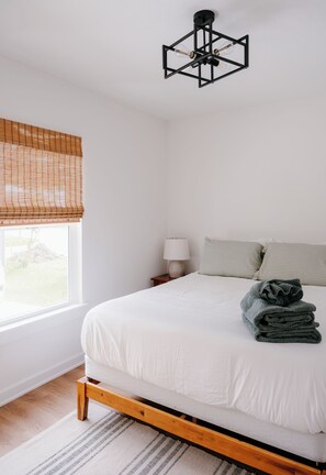A bedroom with a bed, a bedside lamp, a window with blinds, and a hanging light fixture. - Bright and Cozy St. Augustine Home near Downtown (St. Augustine)