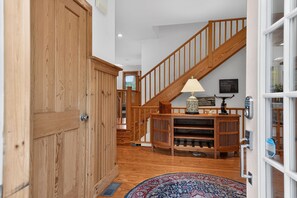 A wooden staircase leading to an upper level, a wooden door, a patterned rug, and a wall-mounted lamp. - Lakefront Catskills Retreat | Dock & Sunsets (Deposit)