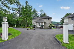 A two-story house with a driveway leading to a gated entrance, surrounded by trees and a well-maintained lawn. - Lakefront Catskills Retreat | Dock & Sunsets (Deposit)
