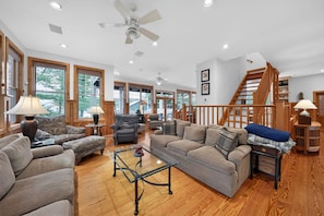 A spacious living room with a wooden floor, a ceiling fan, and a staircase leading to an upper level. - Oquaga Lakefront | Dock, Kayaks & Sunsets (Deposit)