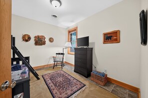 A hallway with a staircase, a television, a dresser, a chair, a rug, and a basket. - Oquaga Lakefront | Dock, Kayaks & Sunsets (Deposit)