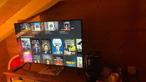 A television displaying various TV shows and movies with their titles and availability times. - Pink Room in a Wooden Chalet (Demi-Quartier)