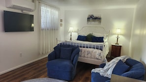 A bedroom with a bed, two bedside lamps, a chair, a television, and a painting on the wall.