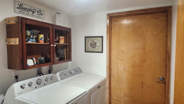 A laundry room with a wooden cabinet containing various cleaning supplies, a white washing machine, and a wooden door.