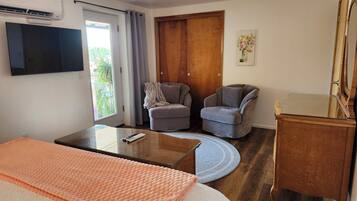 A hotel room with a bed, two armchairs, a small table, a TV, a wooden wardrobe, and a window with curtains.