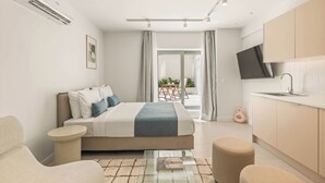 Una habitación de hotel moderna con cama, una zona de estar, kitchenette y un televisor montado en la pared.