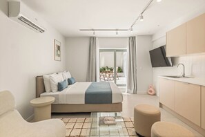 Quarto de hotel moderno com cama, área de estar, cozinha compacta e televisão na parede.