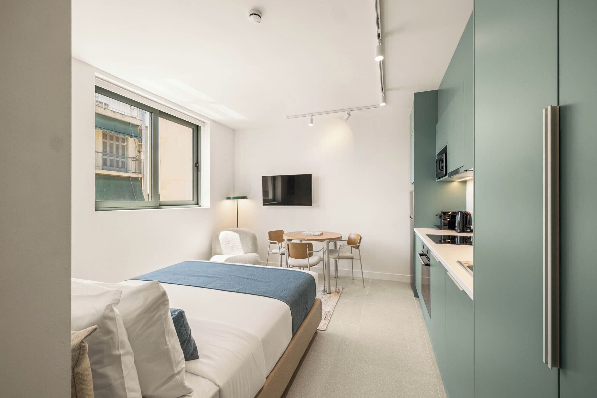 Ein Hotelzimmer mit Bett, Schreibtisch, Fernseher und einer Küchenzeile.