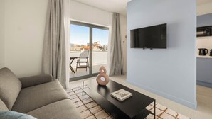 A modern living room with a sofa, a coffee table, a flat-screen TV, and a view of the city through a large window.
