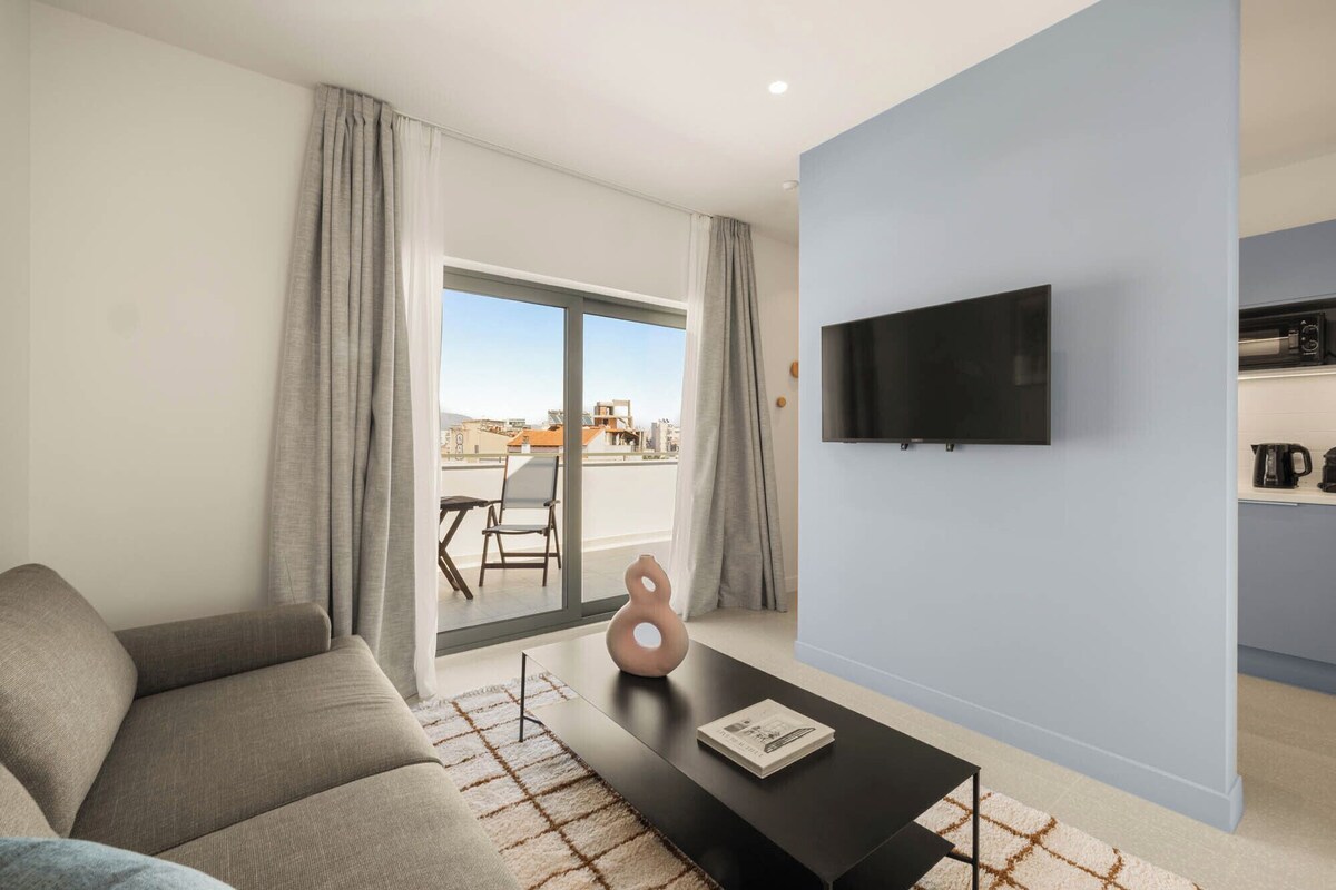 Uma sala de estar moderna com sofá, mesa de centro, televisão de tela plana e vista da cidade por uma grande janela.