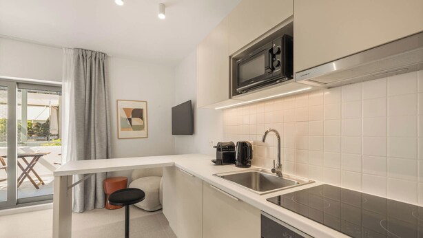 A modern kitchen with a microwave, sink, and stove. There is a bar stool and a window with curtains.