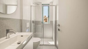 Un baño moderno con ducha envuelta en vidrio, bañera independiente y retrete.