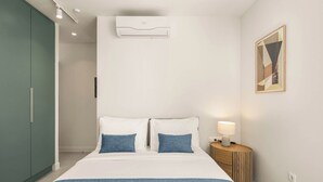 A hotel room with a bed, a bedside table with a lamp, an air conditioning unit, a wardrobe, and a framed picture on the wall. - Kera by Zoia Living (Athens)