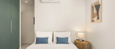 Habitación de hotel con cama, mesita de noche con lámpara, equipo de aire acondicionado, armario y un cuadro en la pared.