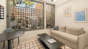 A modern living room with a sofa, a coffee table, a dining table, and large windows with a view of greenery. - Kera by Zoia Living (Athens)