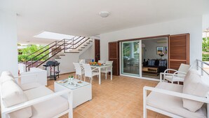 A sunlit patio with a dining table, chairs, and a grill. - Cosy Beach Apartment, Cala Sant Vicenc (Pollença)