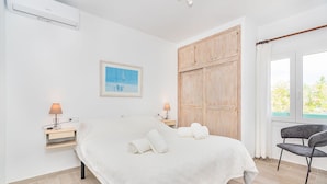 A hotel room with a bed, two bedside lamps, a wooden wardrobe, a framed picture, and a window with curtains. - Cosy Beach Apartment, Cala Sant Vicenc (Pollença)