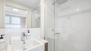 Ein modernes Badezimmer mit Duschkabine aus Glas, Waschbecken mit Spiegel und Pflegeprodukten.
