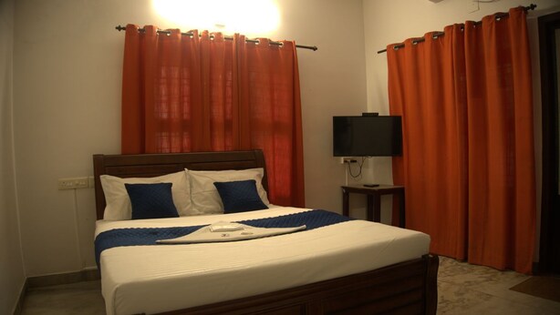 A hotel room with a bed, curtains, a television, and a bedside table. - Hotel Aiden Residency Aluva (North Paravur)