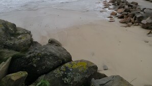 Una playa con olas, rocas y cielo nublado.