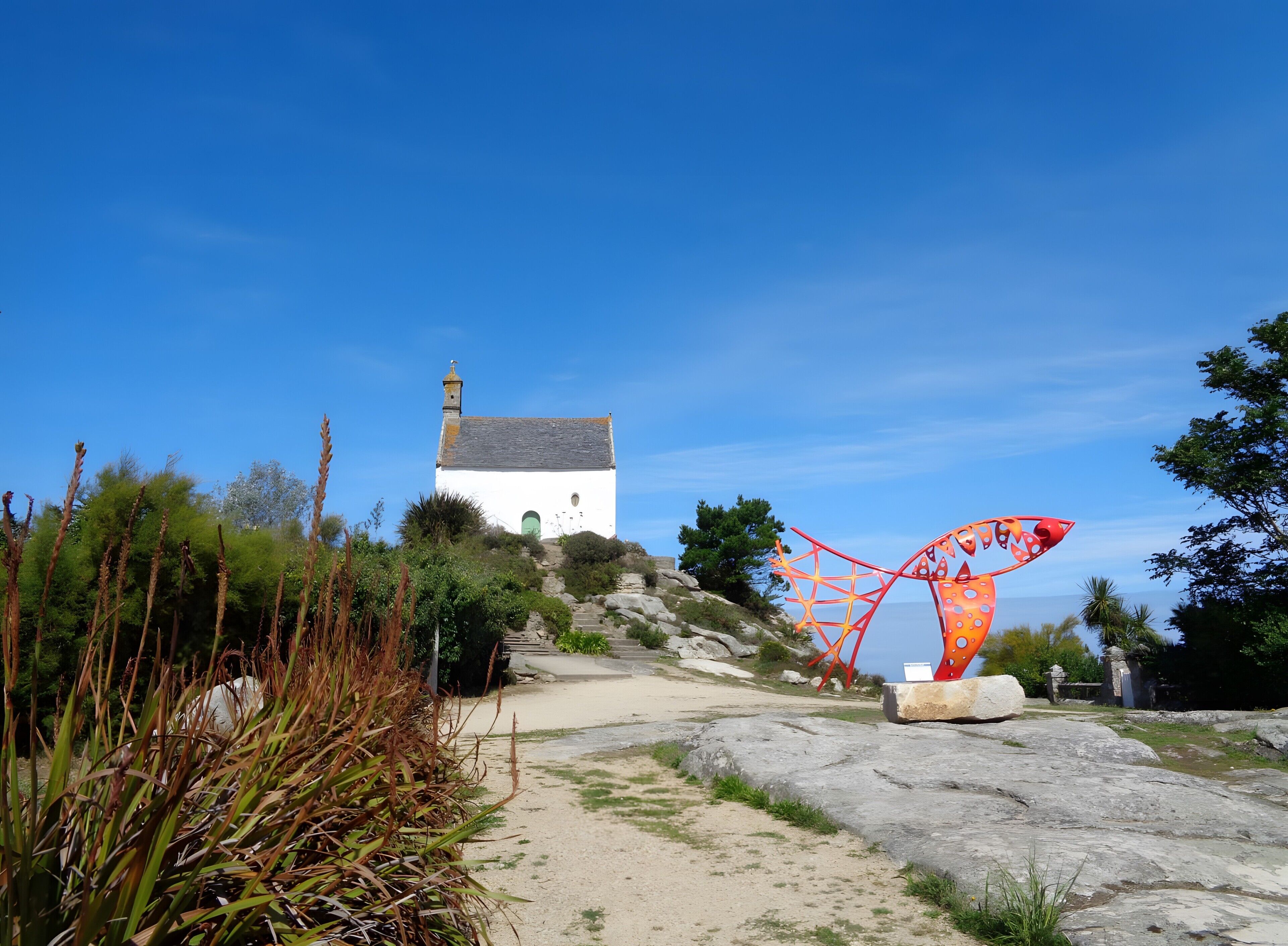 A white building with a bell tower, surrounded by rocky terrain and vegetation.
