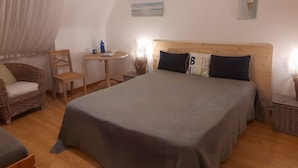 Une chambre à coucher avec un grand lit, une tête de lit en bois, une petite table avec une chaise et un panier en osier.