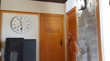 Una habitación con puerta de madera, un reloj en la pared, un refrigerador y piso de baldosas.