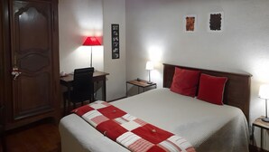 Un dormitorio con cama, escritorio, silla, armario y una pared decorada con cuadros.