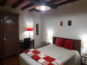 Een slaapkamer met een bed, een bureau, een stoel, een kledingkast en een muur met foto's.
